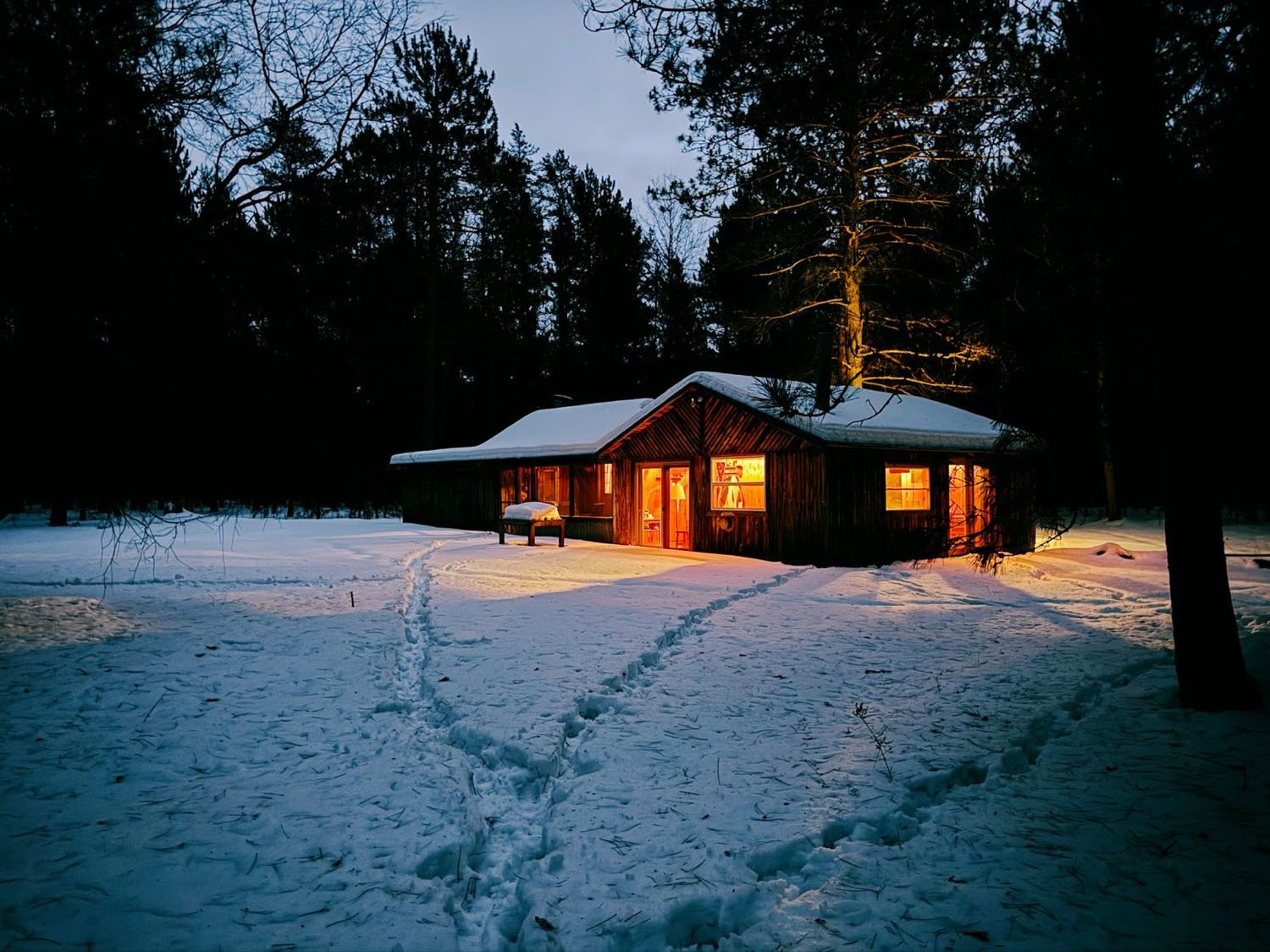 A low building with warmly lit windows in snow at dusk